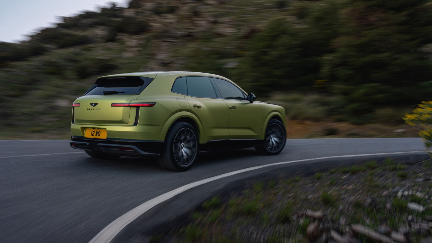 A sleek green Bentley SUV navigating a winding road amidst greenery.