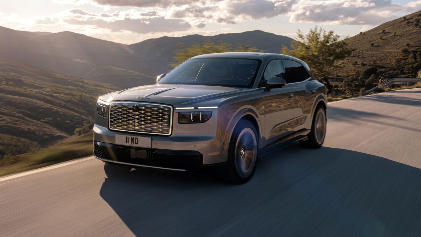Luxury SUV driving on a winding road with mountains in the background during sunset.