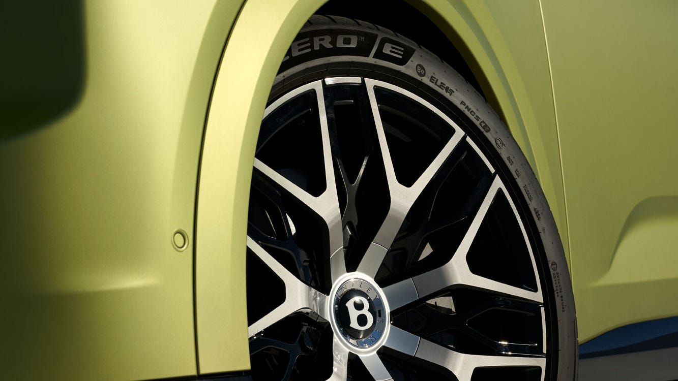 Close-up of a stylish car wheel with a black and silver design on a green vehicle in bright lighting.