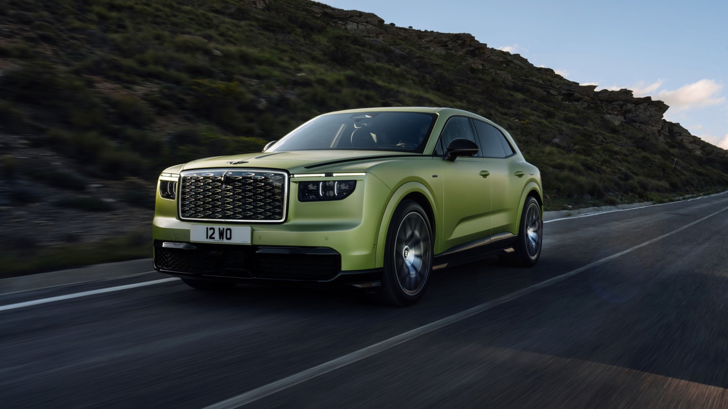A vibrant green luxury SUV driving on a mountainous road under a clear sky.