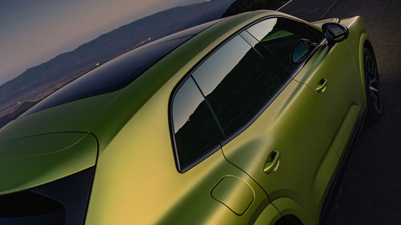 A sleek green SUV parked on a winding road at sunset, showcasing modern design and dynamic curves.