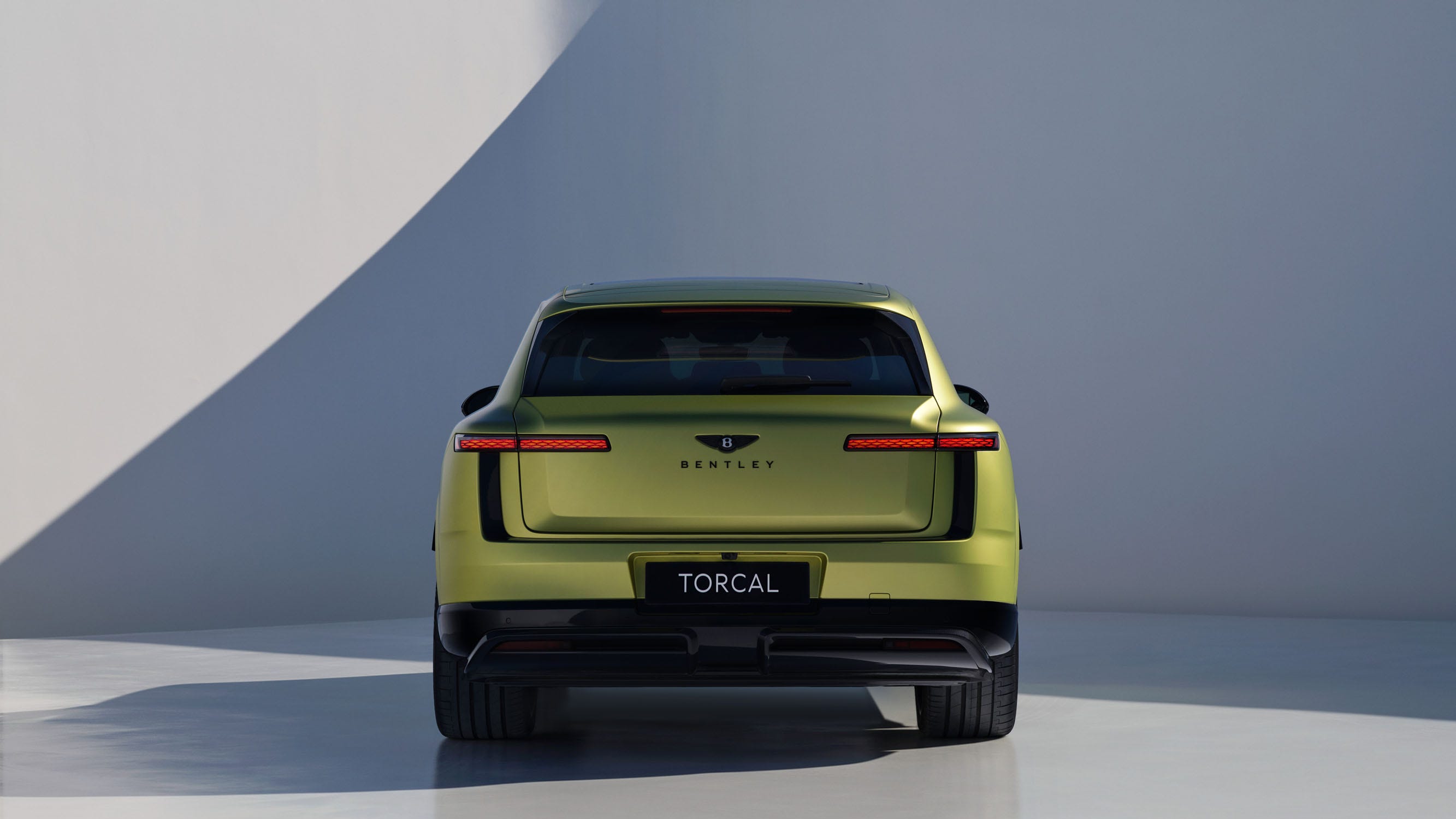 Rear view of a green Bentley SUV in a minimalist setting with soft lighting and a smooth surface.