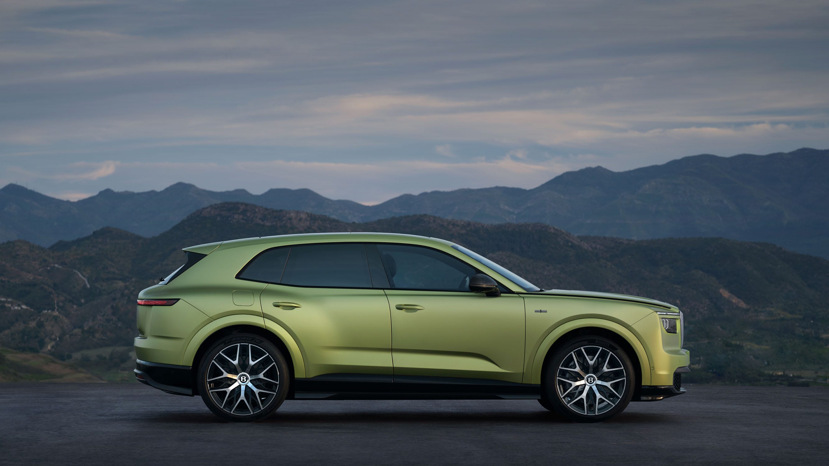 A sleek green SUV with a modern design parked against a mountainous landscape.