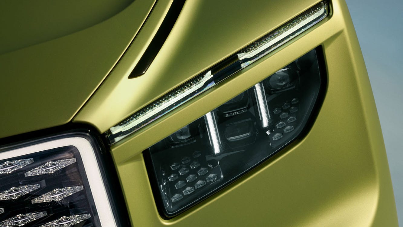 Close-up of a sleek green car's hood, showcasing the headlights and side mirror against a soft gradient background.