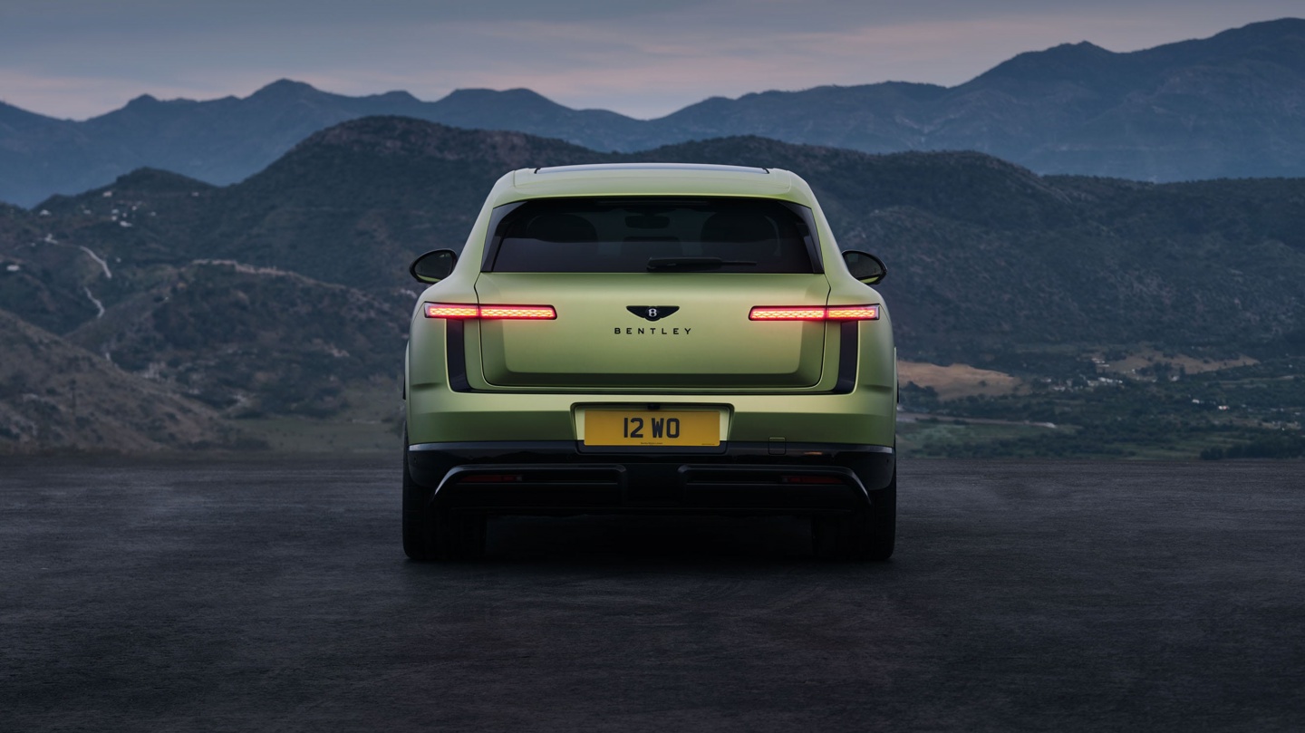 Rear view of a green Bentley SUV parked against a mountainous landscape at dusk.