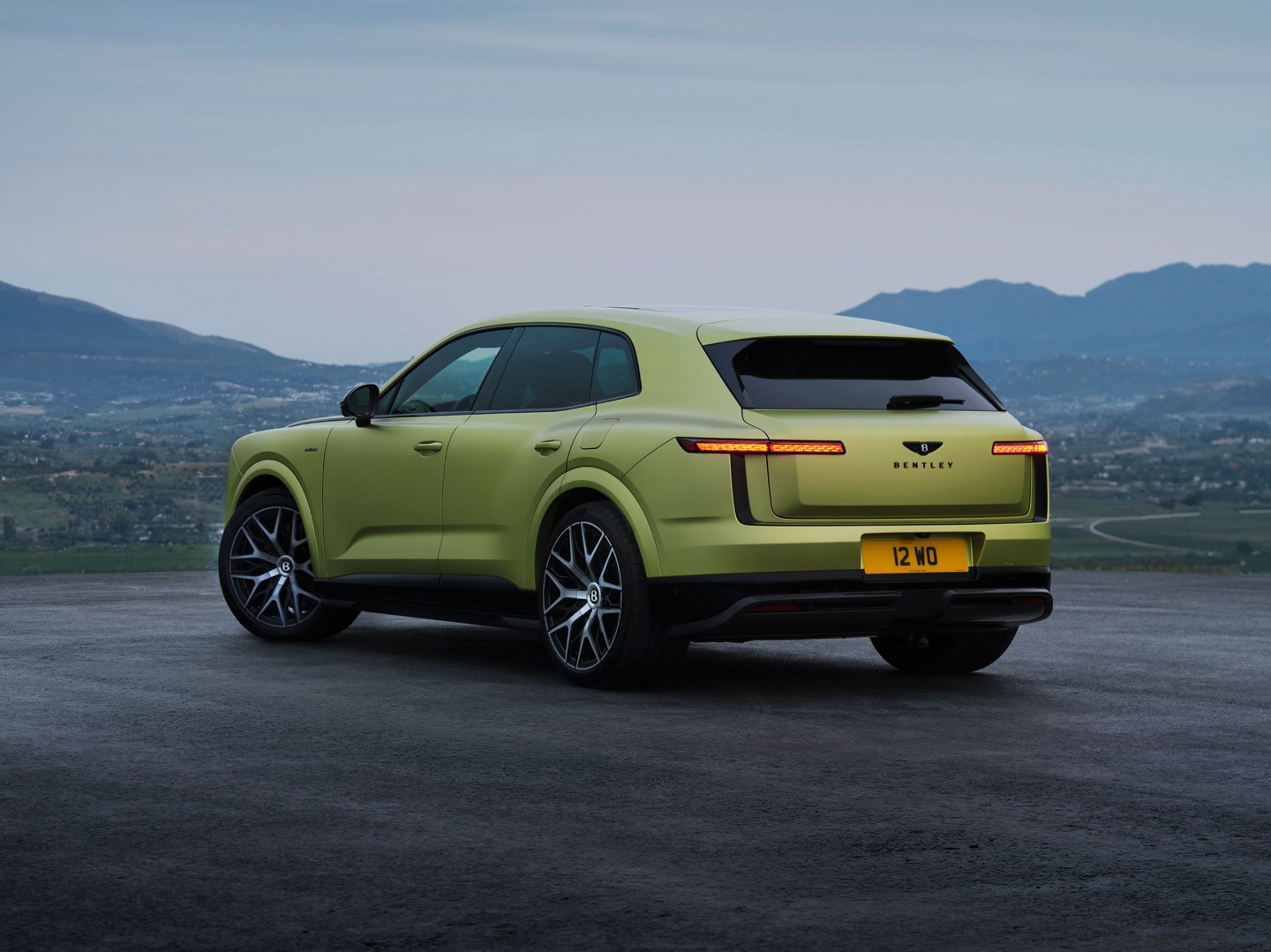 Luxury SUV parked on a scenic overlook with mountains in the background, featuring a distinctive lime green color.